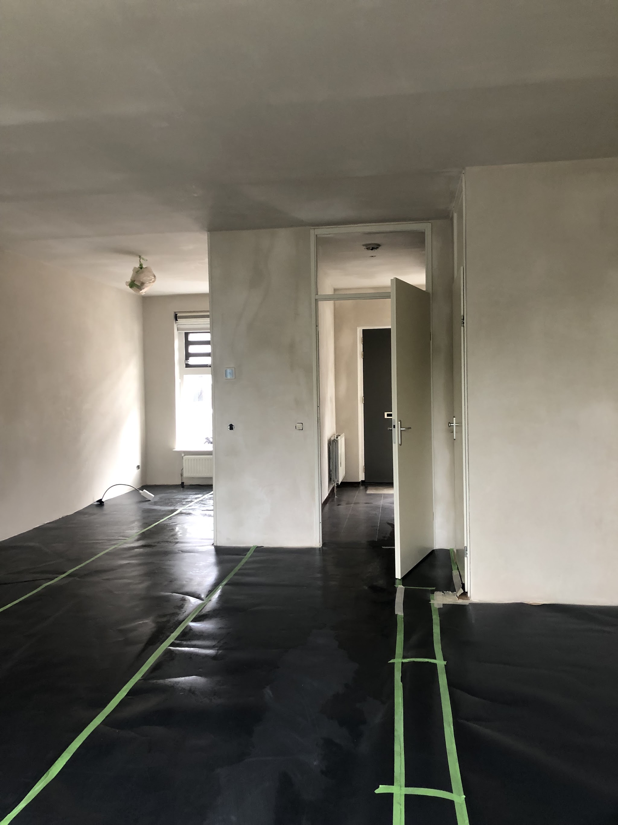 Gestuukte wanden en plafond in een woonkamer en hal, de vloer afgedekt met folie